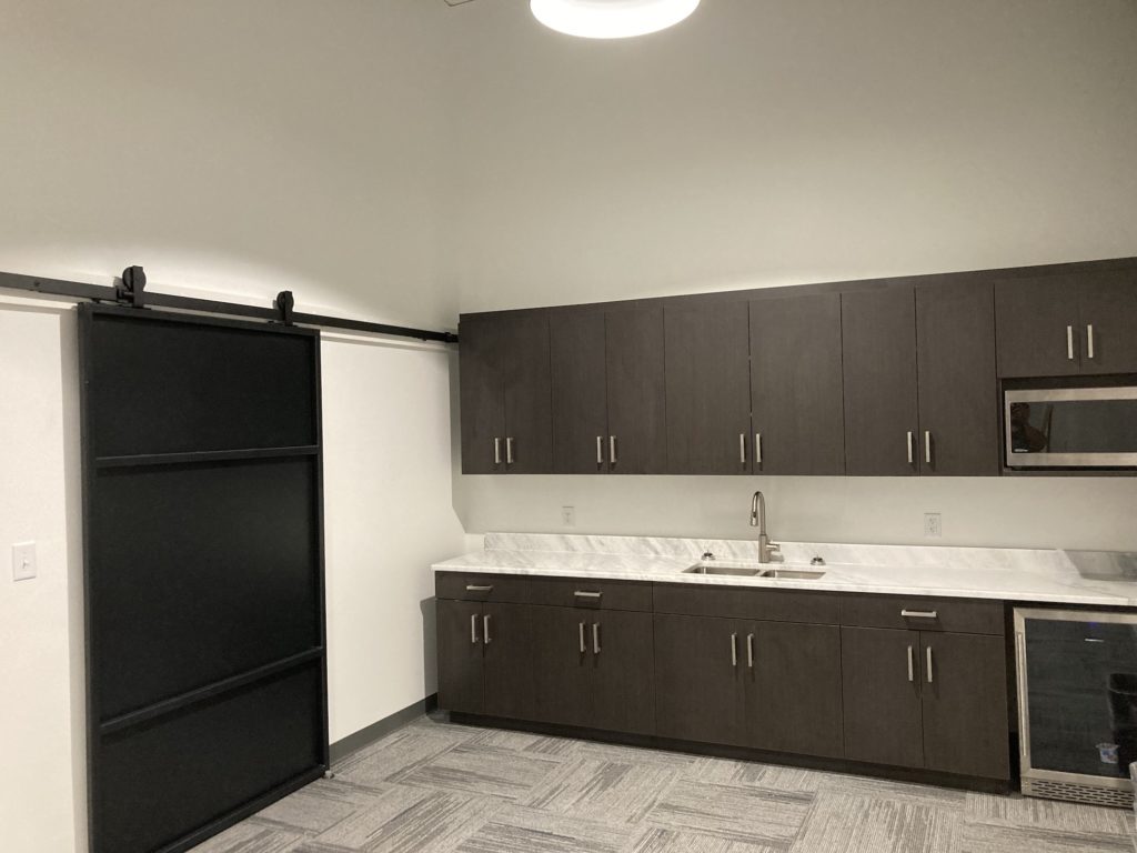 Office kitchen remodel with brown cabinets and sliding, black, steel barn door